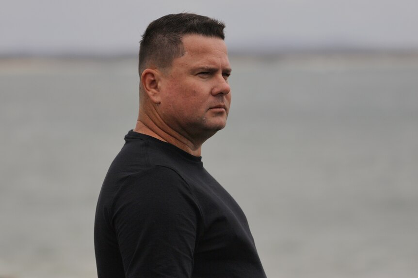 Side profile of a man wearing a black shirt with the ocean behind him.