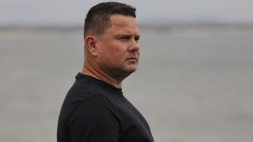 Side profile of a man wearing a black shirt with the ocean behind him.