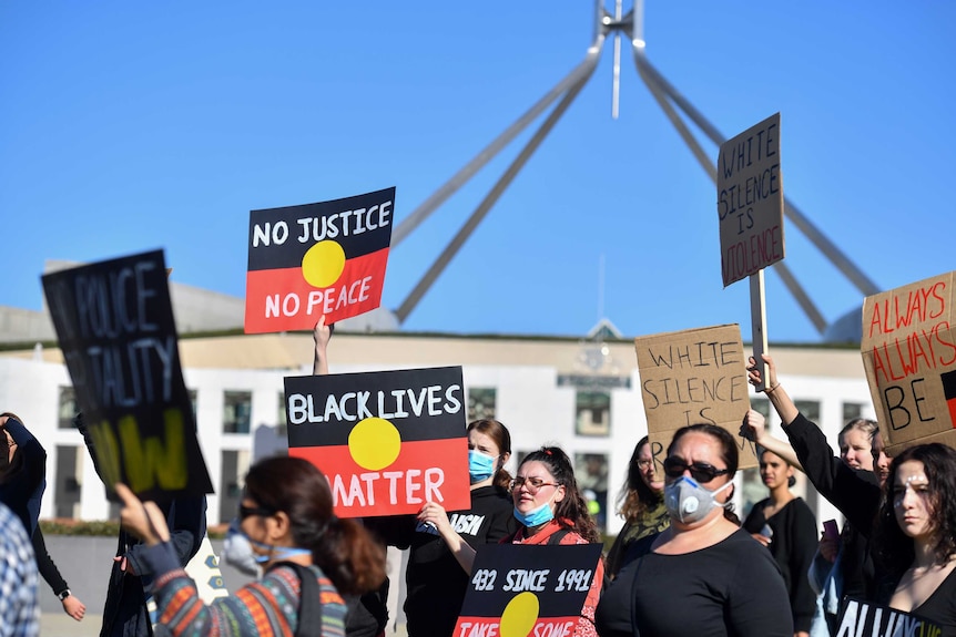 People holding placards with the Aboriginal flag reading "Black Lives Matter" march in front of Parliament House.