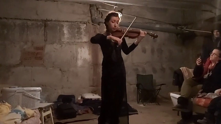 A woman plays the violin in a concrete bunker.