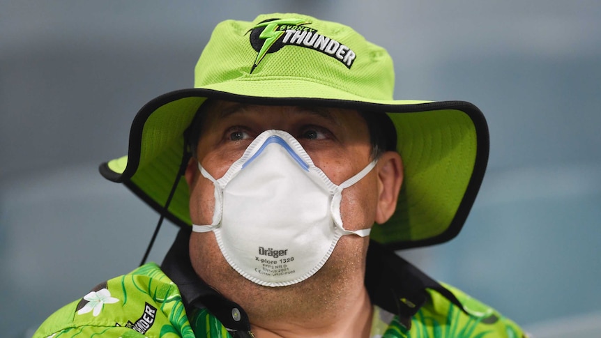 A cricket fan wears a face mask over his mouth and nose in thick smoke at Manuka Oval