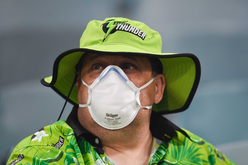 A cricket fan wears a face mask over his mouth and nose in thick smoke at Manuka Oval