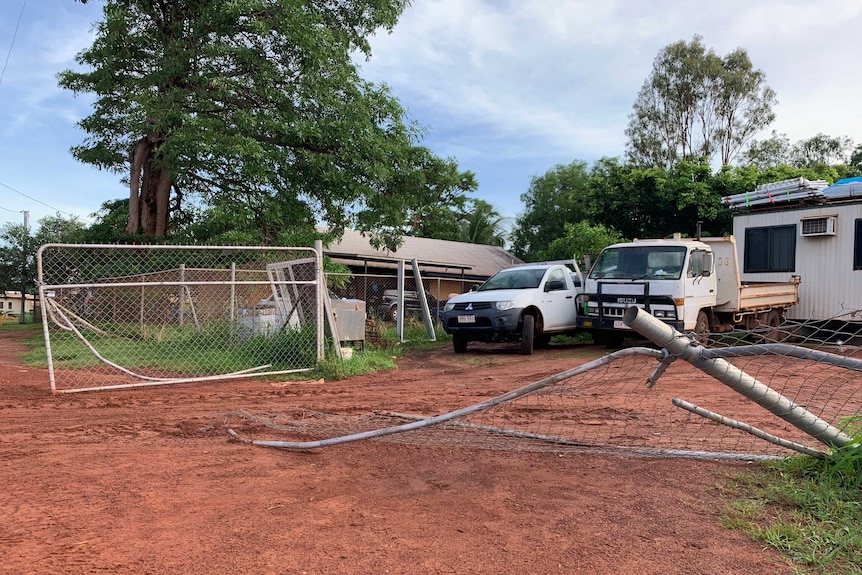 A fence is torn down, with two vehicles behind the fence near a demountable office.