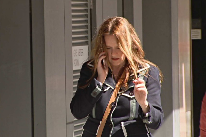 A woman with long auburn hair walking along talking on a mobile phone.