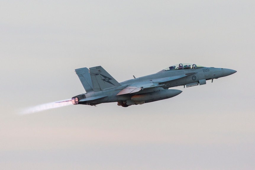 A military fighter jet takes off at a steep angle with flames coming out of the engine's afterburners.