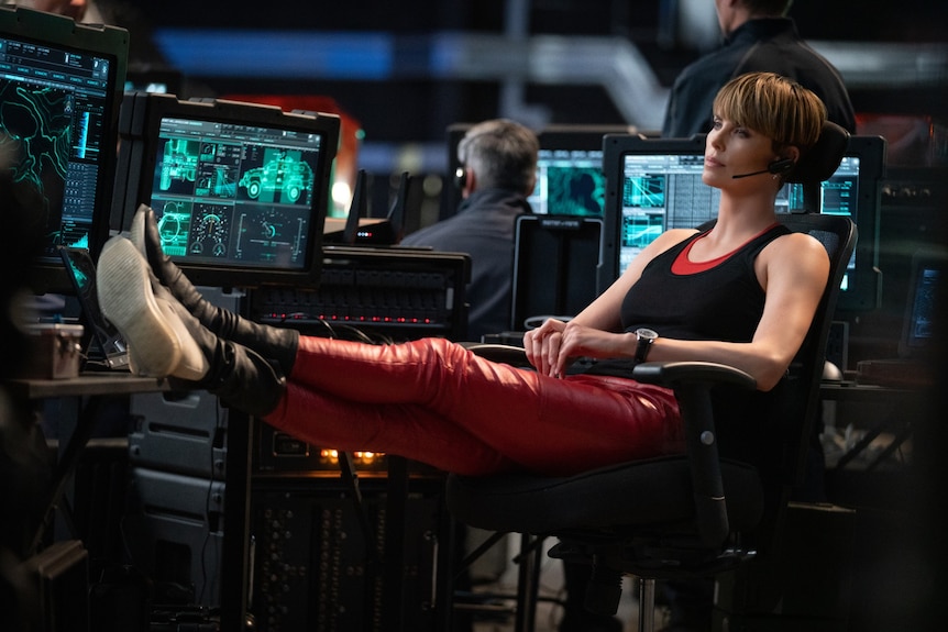 Charlize Theron leaning back in her chair with her feet up on a desk in Fast and Furious 9