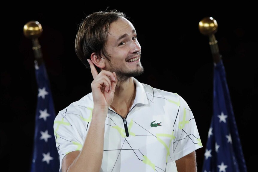 Daniil Medvedev smiles and points to his ear with one finger