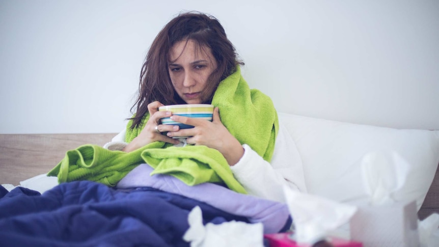 A woman sits in bed looking sick