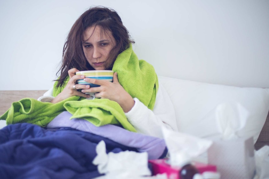 A woman sits in bed looking sick