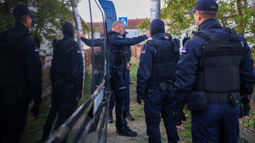 A police officers holds out his arm and points as other police officers gather before a search in Serbia
