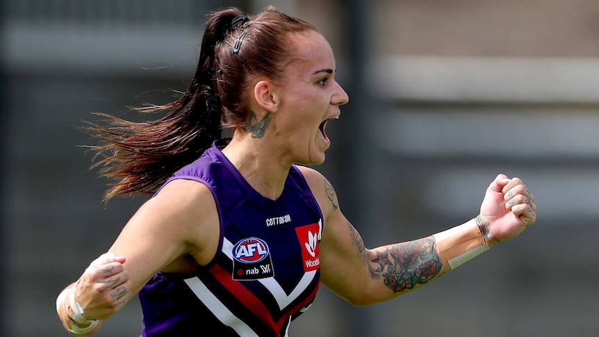 A Fremantle AFLW player pups her fists as she celebrates a goal against the Suns.