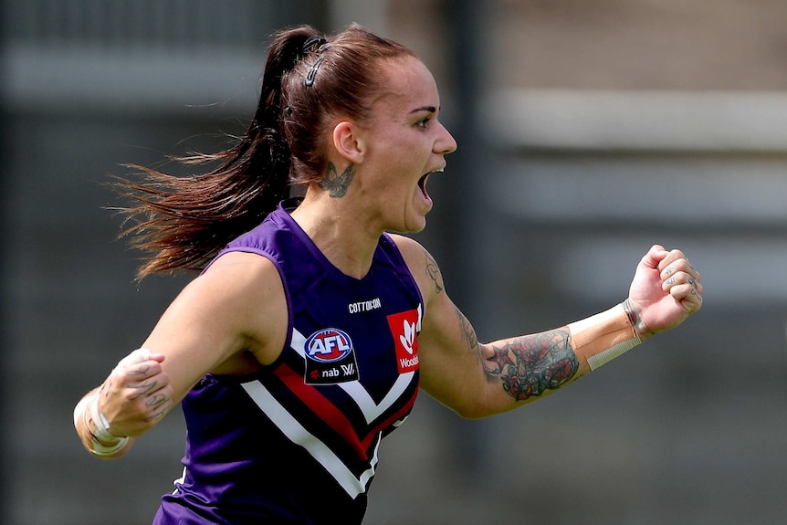 A Fremantle AFLW player pups her fists as she celebrates a goal against the Suns.