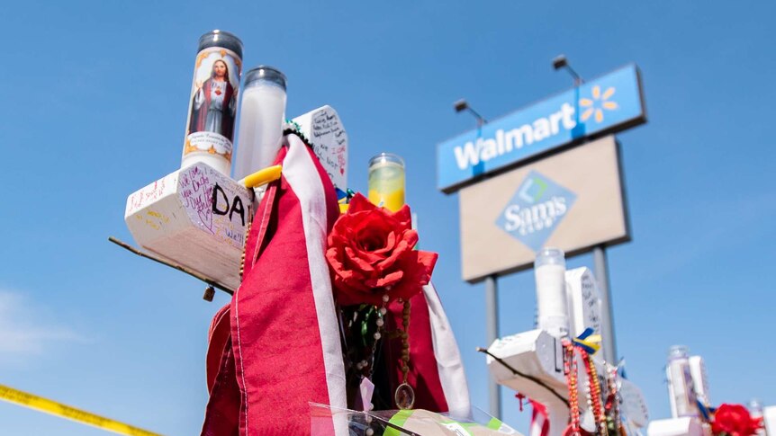 A cross covered with flowers and love notes sits in the parking lot of the Walmart in El Paso, Texas.