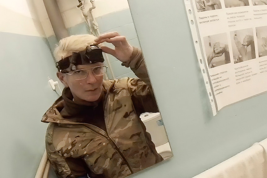 A mirror reflection of medic Yuliia Paievska with a body cam on her forehead. She is reaching the camera with one of her arms. 