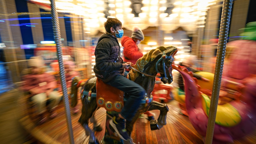 Children, some wearing face masks, enjoy a carousel ride at a Christmas fair