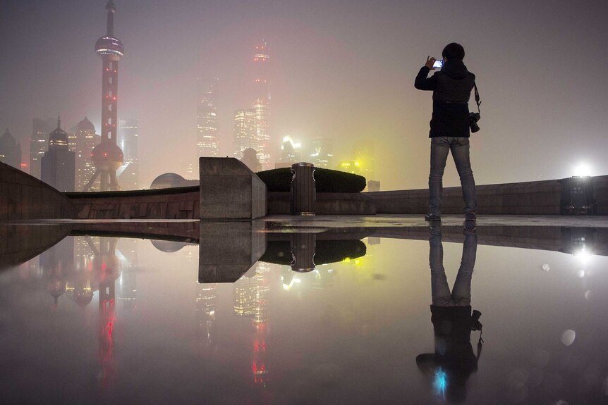 A man uses his phone to take a picture of Shanghai's financial area engulfed in smog at night.
