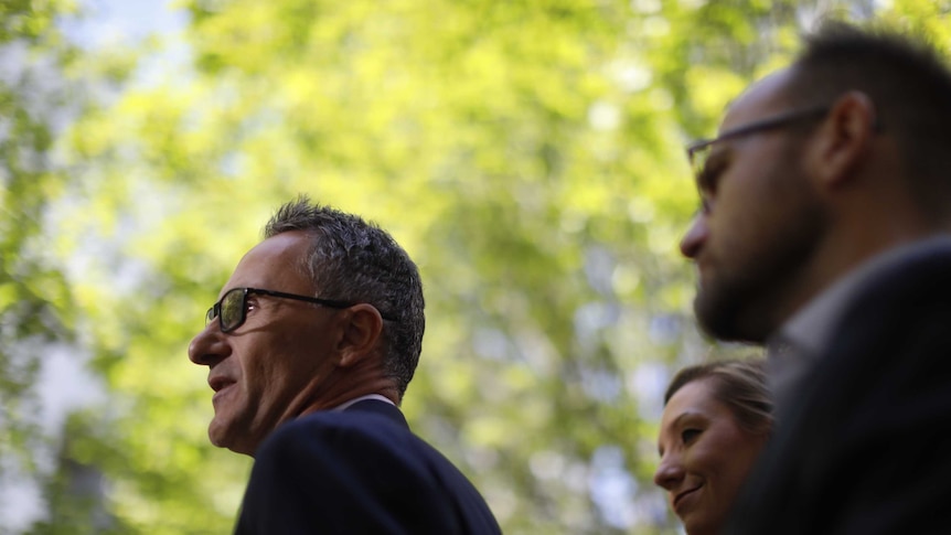 Adam Bandt and Larissa Waters stand behind Richard Di Natale in a courtyard at Parliament House