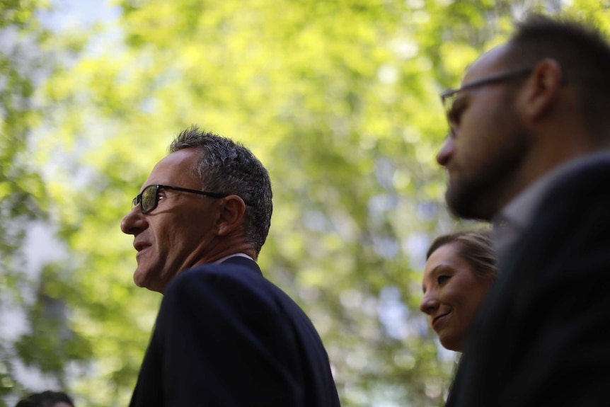 Adam Bandt and Larissa Waters stand behind Richard Di Natale in a courtyard at Parliament House