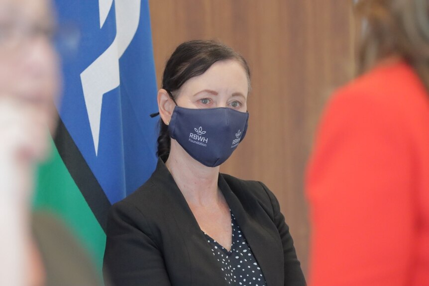 Health Minister Yvette D'Ath wears a mask at the daily COVID media conference, with flags in background.