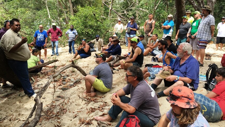 A group of workshop participants sit on creek bank while welcomed to country by indigenous leader
