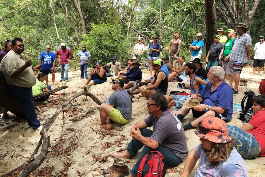 A group of workshop participants sit on creek bank while welcomed to country by indigenous leader