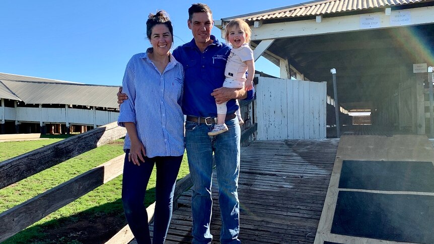 Clare and David Lee pose outside a wool shed with their young daughter.
