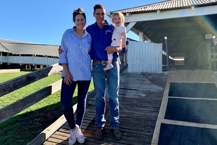 Clare and David Lee pose outside a wool shed with their young daughter.