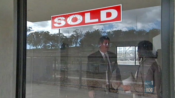 Real estate agent and client behind a window with a 'Sold' sign