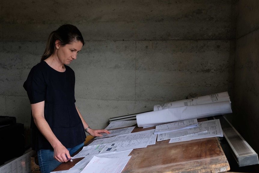 Jane stands at a drafter's table and looks at building plans.