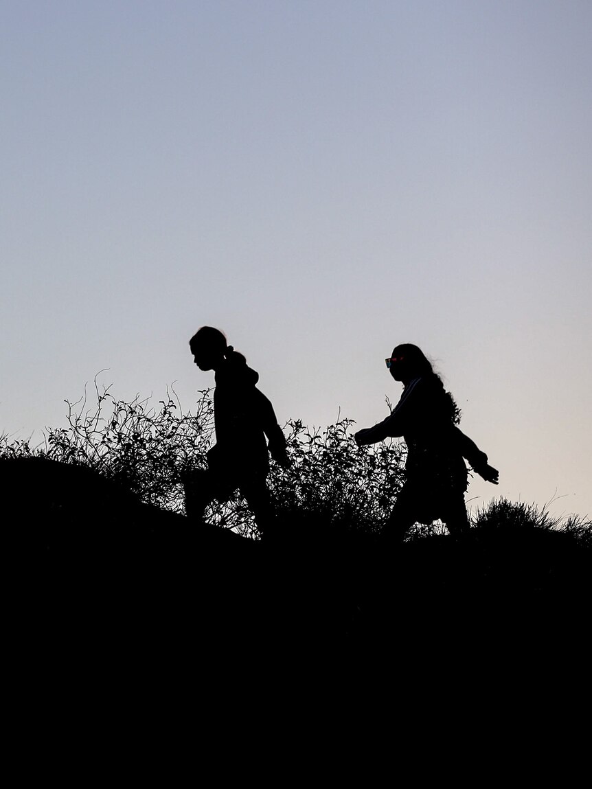 Five young Aboriginal women are silhouetted against the early evening sky walking across a hill