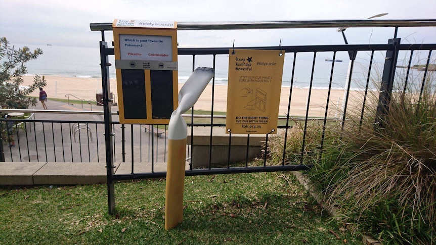 A yellow bin with two slots on a fence over looking a beach