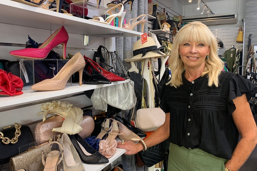 A blond woman stands next to a rack of shoes in a shop