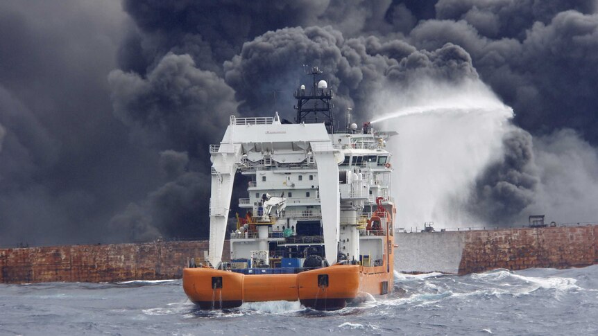 A ship sprays water onto a tanker that is on fire. Smoke billows from the tanker.