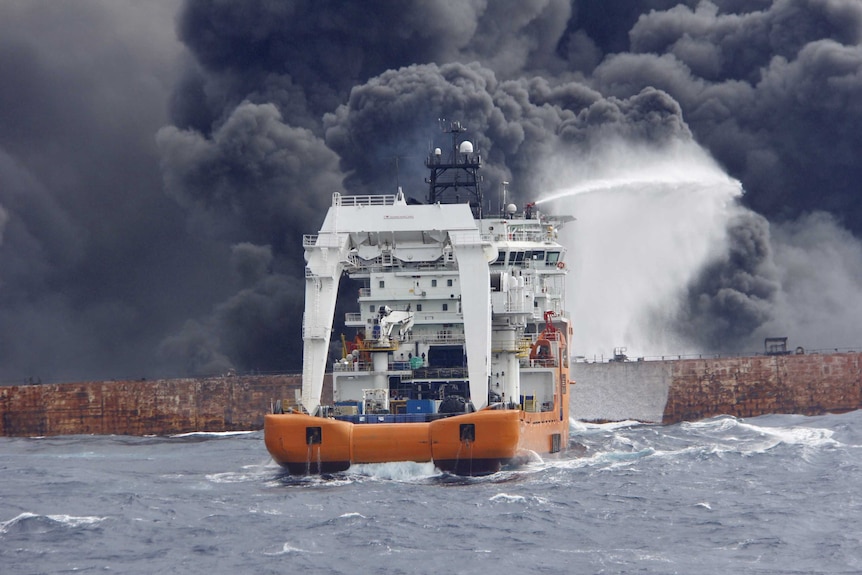 A ship sprays water onto a tanker that is on fire. Smoke billows from the tanker.