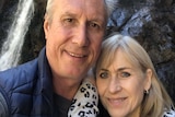 A man and woman in a selfie in front of a waterfall.