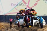 A car full of people standing against a fence with a map of Rafah overlaid 