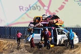 A car full of people standing against a fence with a map of Rafah overlaid 