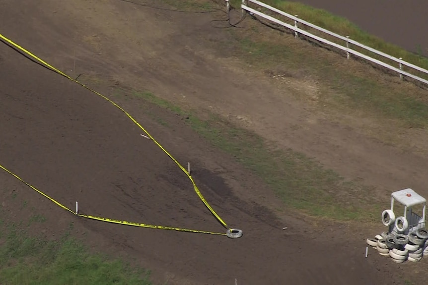 An aerial view of yellow tape over a dirt motorbike track, with a pile of tyres nearby.