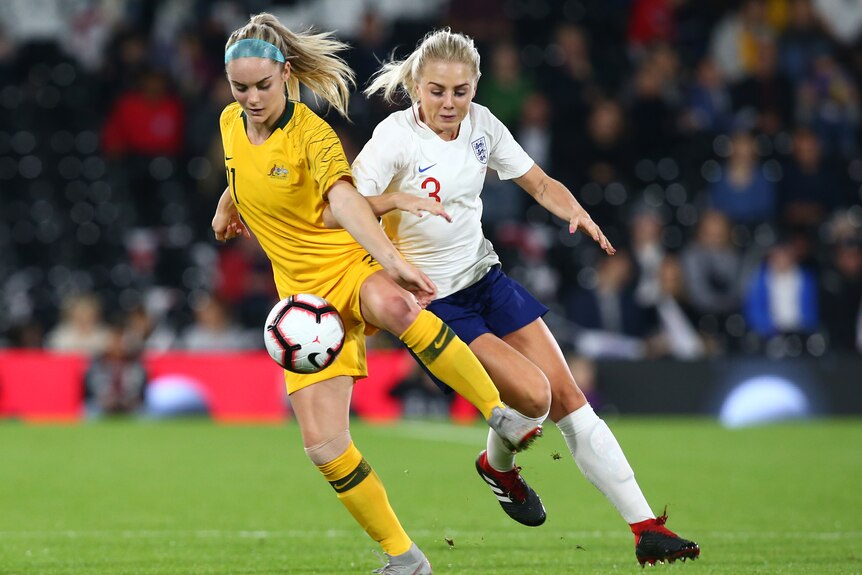 Matildas player Ellie Carpenter competes with Lionesses player Alex Greenwood for the ball during a football match.