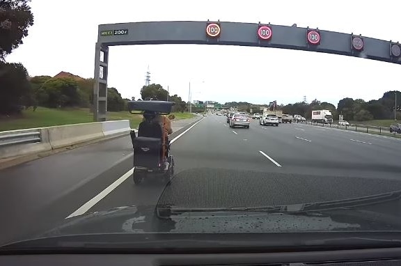 A mobility scooter is driven down a freeway, with traffic nearby.