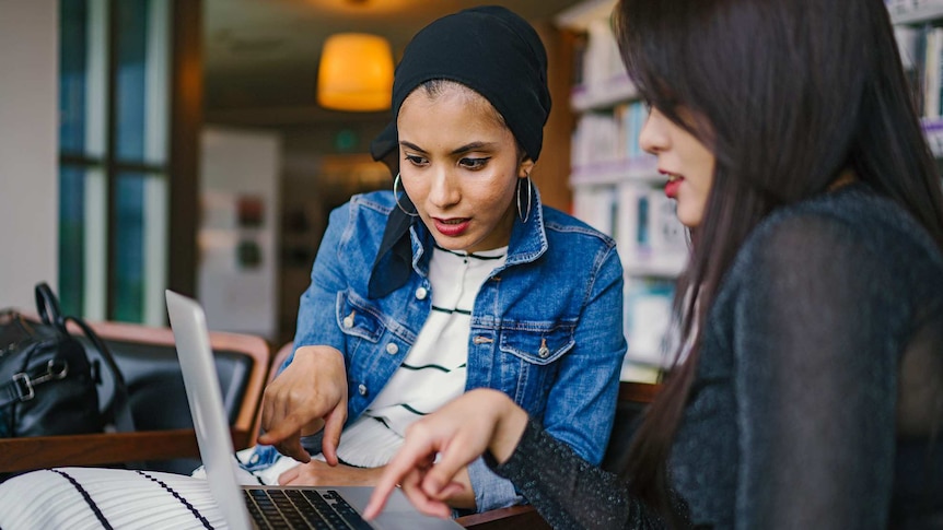 Two women point at a laptop screen, for a story about JobKeeper and annual leave.