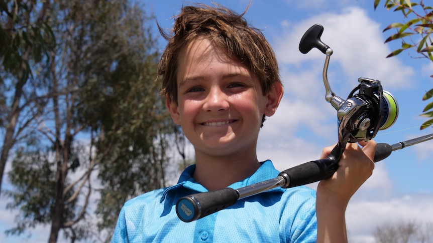 A young boys holds a fishing rod about to cast smiling at the camera