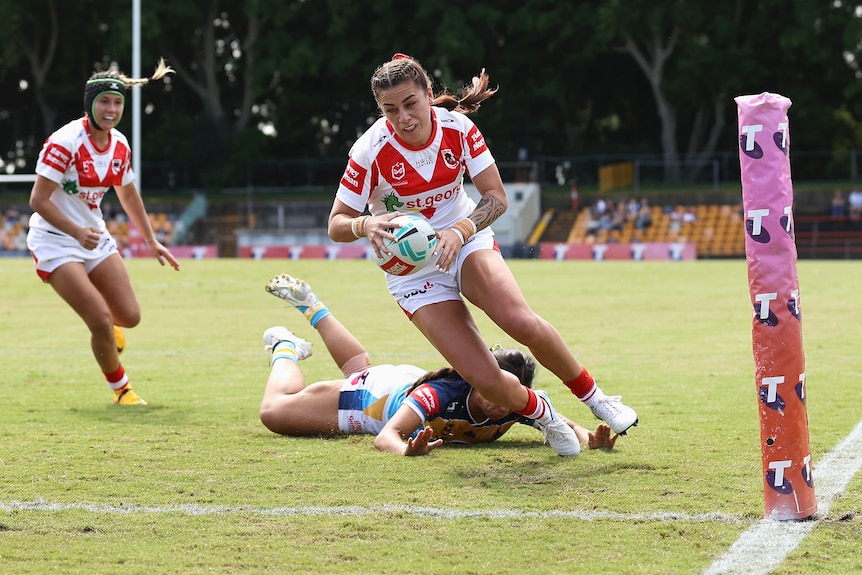 A woman in white and red prepares to touch a ball down for a try