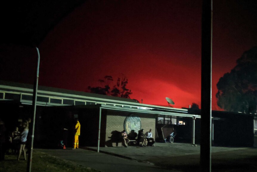 A red glow from the fire can be seen in the sky in the distance above a building.