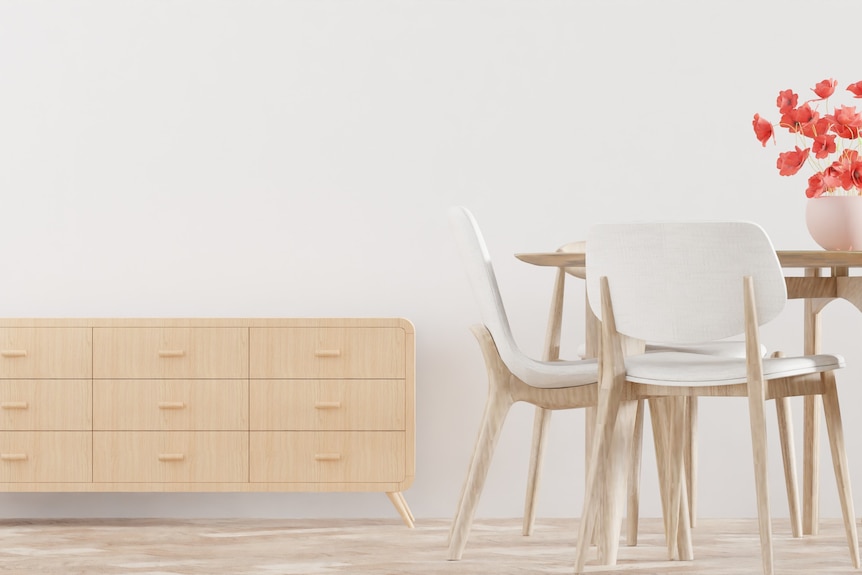 A light wooden furniture unit rests against a white wall, a table beside it.