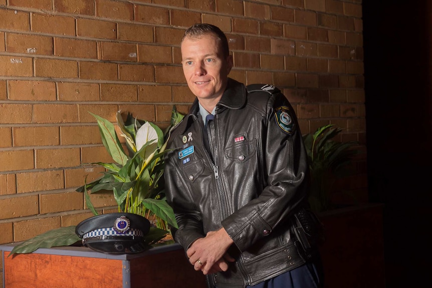 A police officer in uniform standing next to a pot plant and wearing a white ribbon