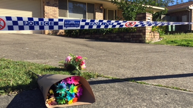 A low-set brick house with flowers outside, police tape cordons off the yard.