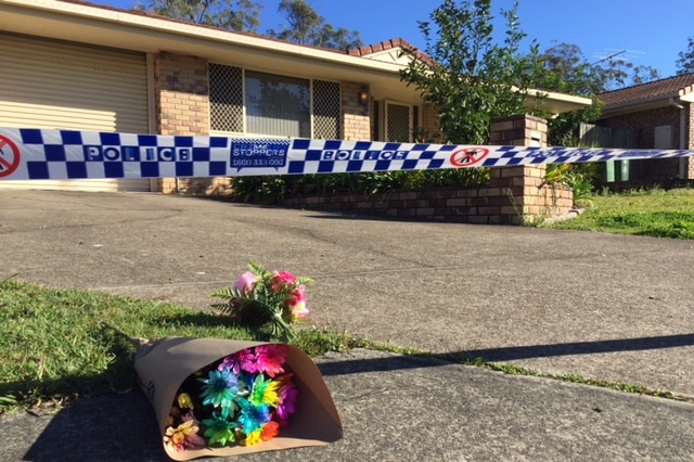 A low-set brick house with flowers outside, police tape cordons off the yard.