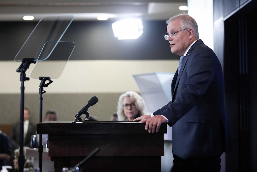 Scott Morrison reads from a teleprompter at the National Press Club. Laura Tingle sits behind him.