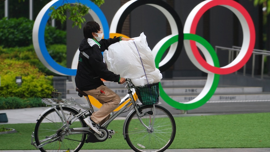  A man wearing protective masks rides a bicycle in front of he Olympic Rings in Tokyo.